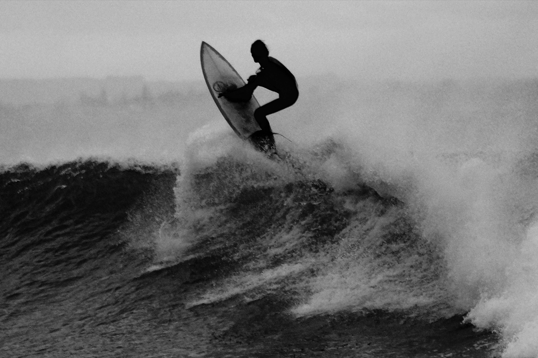 Surfeur en l'air au-dessus d'une vague, noir et blanc