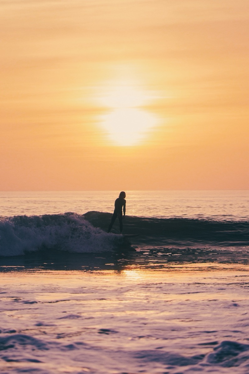 Silhouette d'un surfeur sous un soleil couchant orangé
