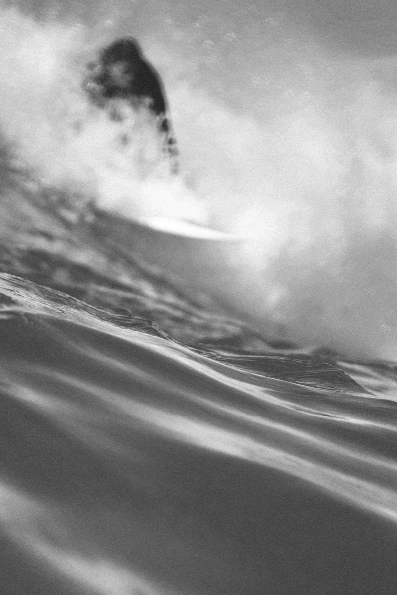 Surfeur flou derrière la houle, au ras de l'eau, noir et blanc